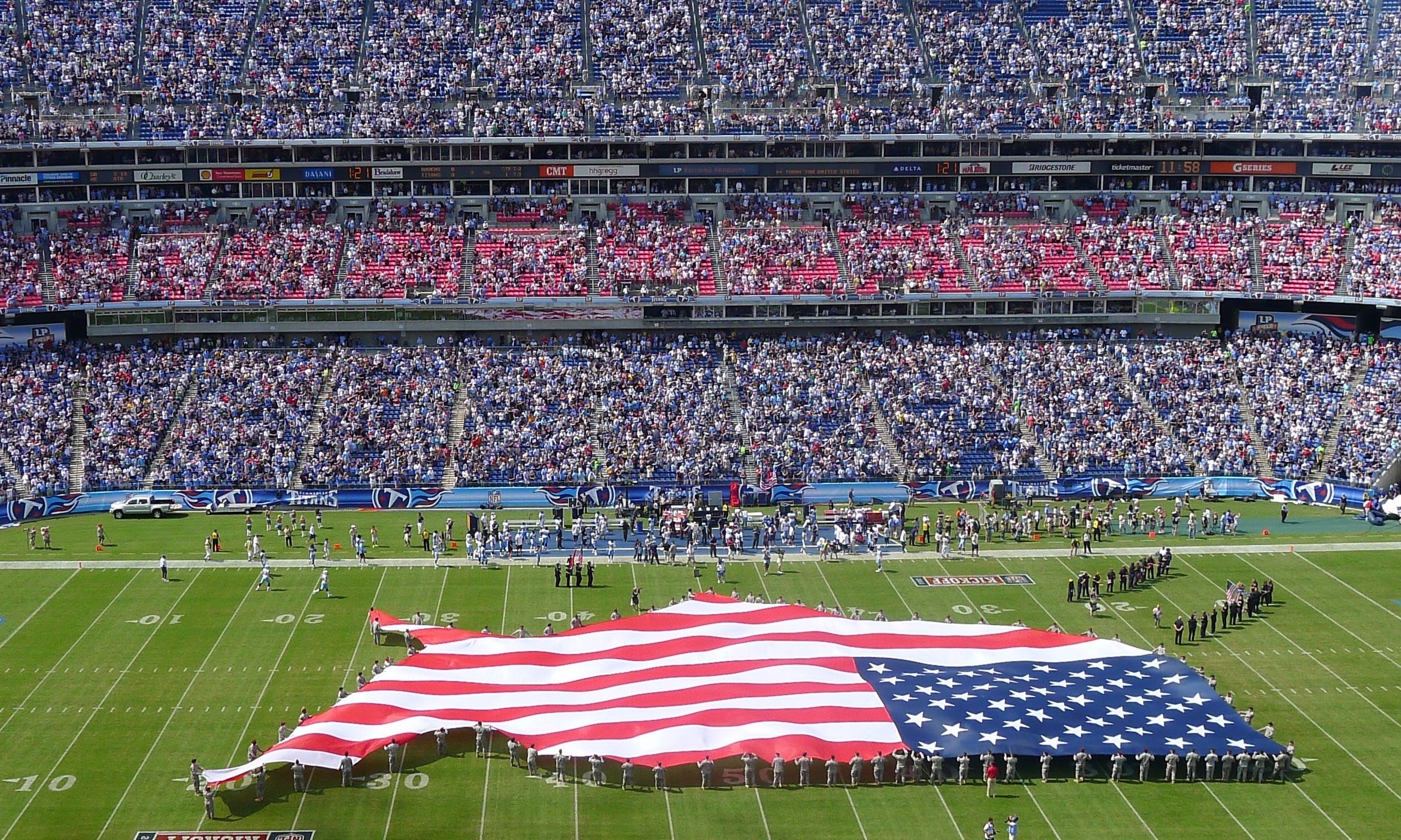 A large American flag in the shape of the United States is stretched out across a football field